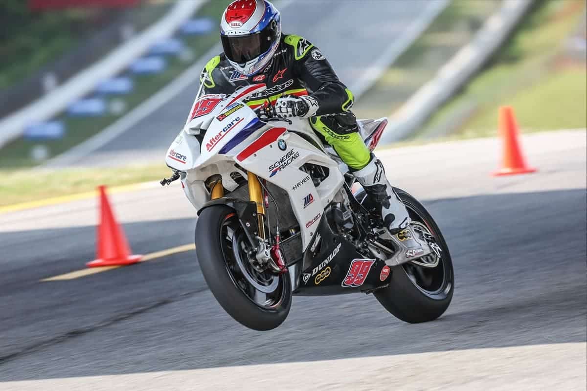 sponsored-athletes-motorcycle1 A professional motorcycle racer in black and neon performing a "wheelie" on a white BMW racing bike during a track session.